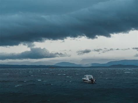 Small Boat Sailing In The Stormy Ocean Under The Dark Cloudy Sky Stock