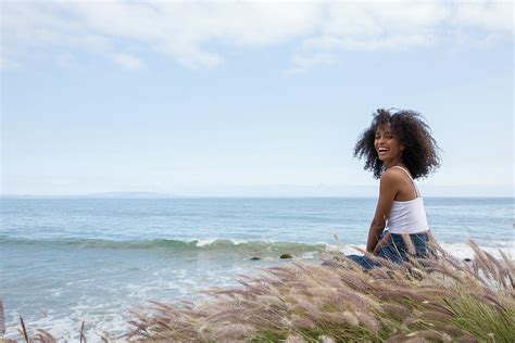 Lifestyle Portrait Of Black Woman Sitting Laughing By The Ocean