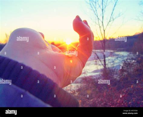 Optical Illusion Of Woman Hand Holding Sun During Sunset Stock Photo