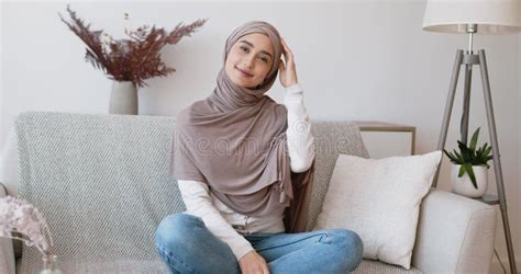 portrait of beautiful arabic woman in hijab sitting on couch in living room and smiling at