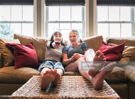 Two Teenage Girls Sitting On A Couch With Their Feet Up Watching Tv