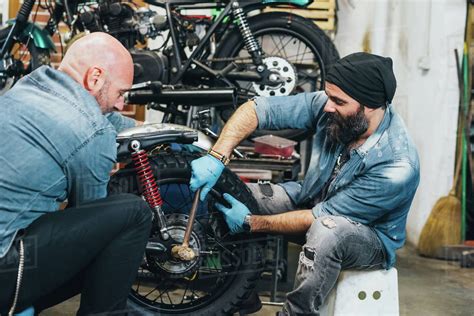 Motorcycle work is the combination of some works of different parts. Two mature men, working on motorcycle in garage - Stock ...