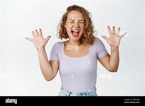 excited blond girl screaming and shaking raised hands shouting with closed eyes showing