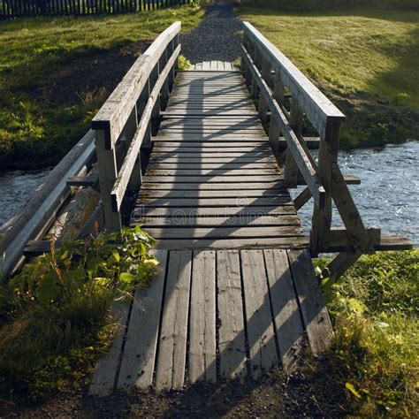 Small Wooden Bridge Over A Small River With Mountains In The Background