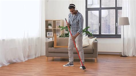 cleaning, housework and housekeeping concept - indian man in headphones with broom sweeping ...