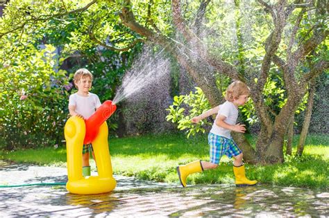 Two Little Kids Playing With Garden Hose And Water In Summer Stock