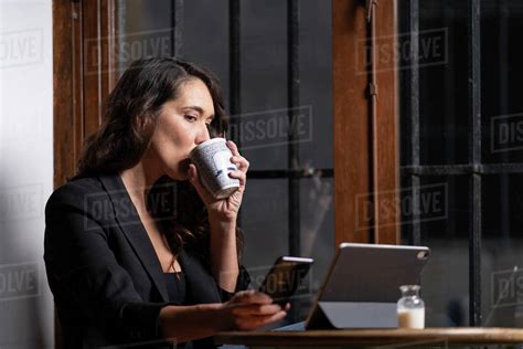side view of beautiful woman sitting at table with tea cup and browsing on mobile phone and in