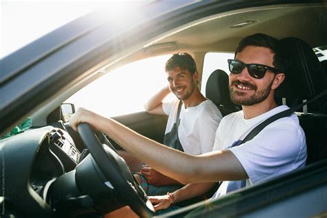 Two Young Man Friends Driving A Car At Sunset Looking At Camera During