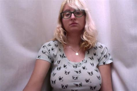 A Woman With Glasses Is Sitting In Front Of A White Curtain And Posing