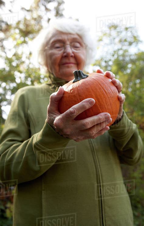 Older Caucasian Woman Admiring Pumpkin Outdoors Stock Photo Dissolve
