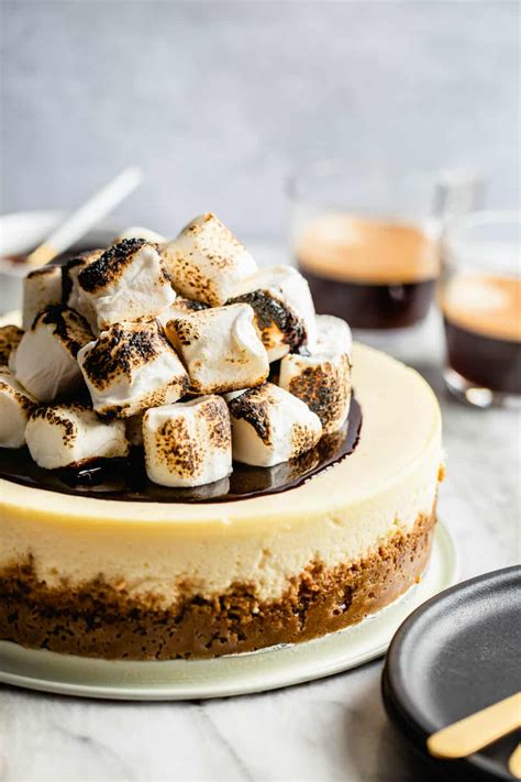 S Mores Cheesecake Topped With Toasted Marshmallows In Front Of Cups Of