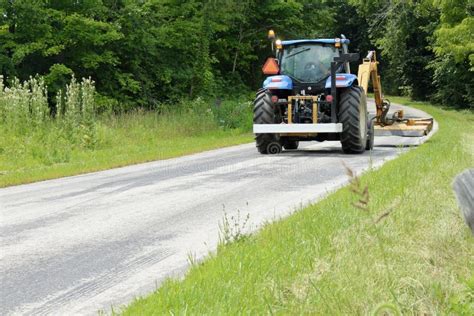 Tractor Mowing The Grass On The Side Of A Country Road Stock Photo