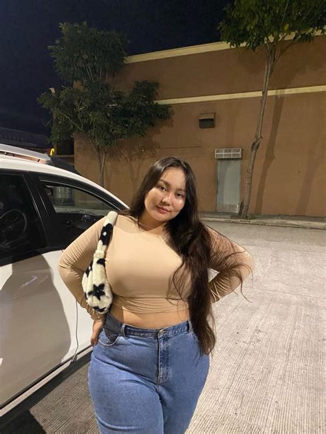 A Woman Standing In Front Of A White Car Wearing High Waist Jeans And A Scarf