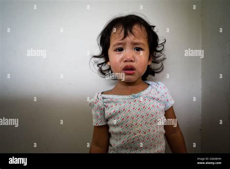 Portrait Of A Cute Thai Girl In Tears Against A White Wall Stock Photo