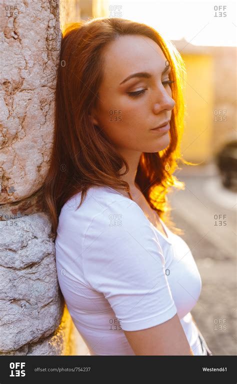 Portrait Of Redheaded Woman Leaning Against Wall At Sunset Stock Photo