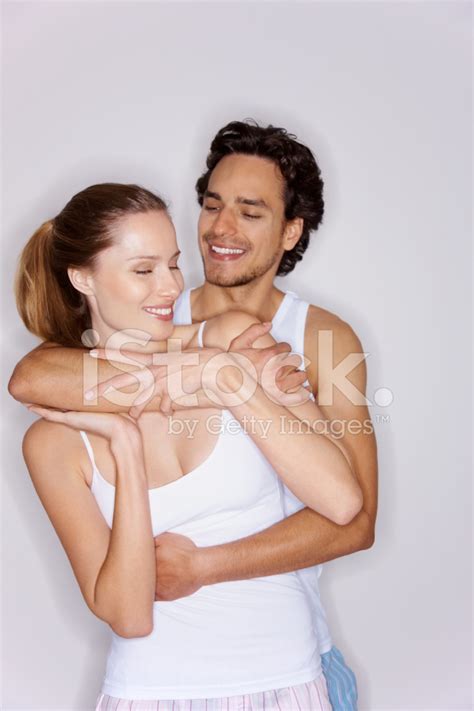 Young Man Hugging A Woman From Behind Against Gray Stock Photo