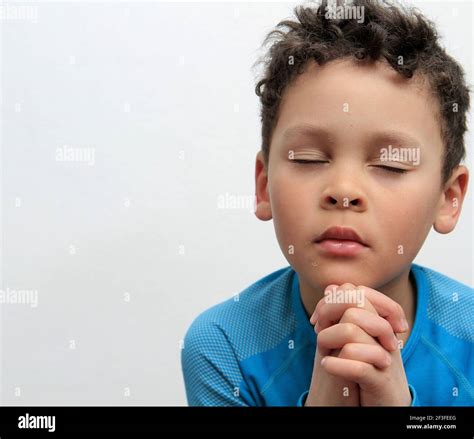 Boy Praying To God With Hands Held Together With Closed Eyes On White