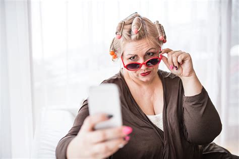 An Attractive Overweight Woman With Sunglasses And Hair Curlers At Home Taking Selfie Stock