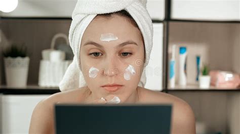 Girl Puts On Face Shine For Skin Attractive Girl With Towel On Her Head In Bathroom Applies