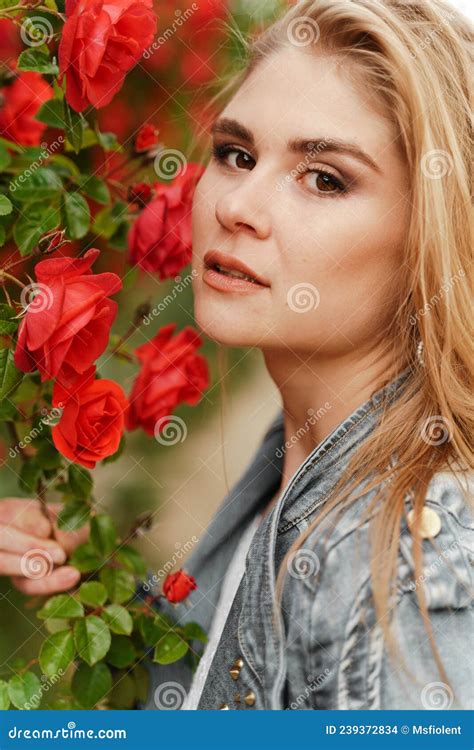 A Cute Blonde Stands Near A Bush With Red Roses Attractive European