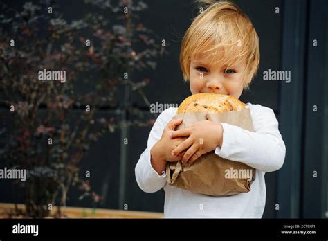 Happy Boy With Blond Hair Holding Crispy Bread In Hands Outdoors On