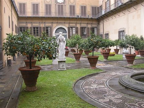 There Are Many Potted Trees In The Courtyard And On The Lawn With Statues