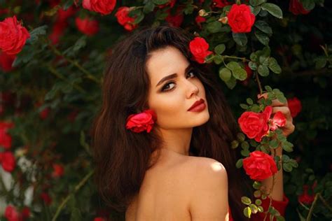 پرتره بیرون از خانه از زن زیبای طبیعی با گل رز قرمز زن شهوانی با گل های رز در مو سبزه زیبا با