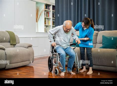 Asian Nurse Assisting Helping Senior Man Patient Get Up From Wheelchair