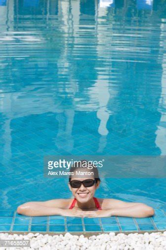 Woman Leaning On Edge Of Swimming Pool Wearing Sunglasses Smiling High