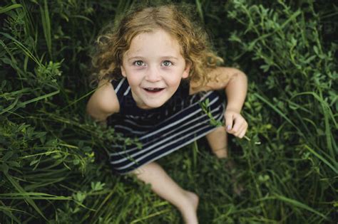 Girl Looking Up At Camera On Green Grassy Field Stock Photo