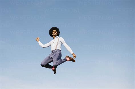 Smiling Man Jumping In The Air Against Blue Sky Stock Photo
