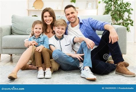 Parents And Two Kids Sitting Near Sofa In Living Room Stock Image