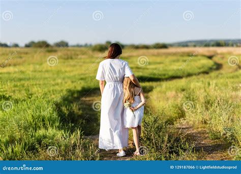 Rear View Of Mother And Daughter Walking By Rural Road Stock Photo