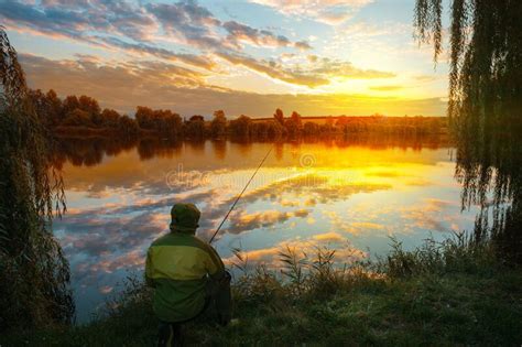 Fisherman Seated By Lake At Sunset Under Dramatic Sky Stock Photo