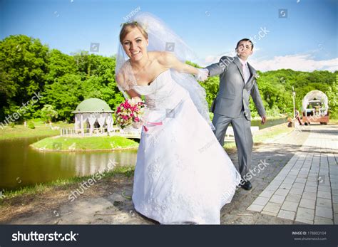 Beautiful Bride Pulling Handsome Groom By Hand At The Park Stock Photo