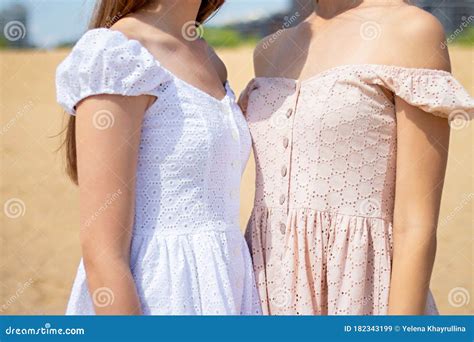 Close Up Of Two Girls In Summer Dresses Stand Together Against The Background Of Beach On Sunny