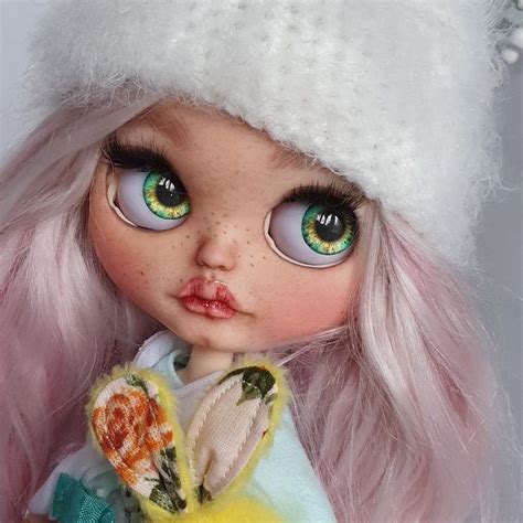 A Close Up Of A Doll With Pink Hair And Green Eyes Wearing A White