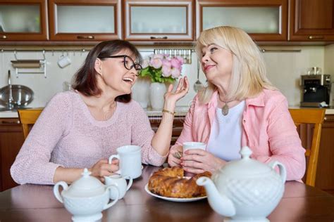 Friends Two Mature Women Drinking Tea With Cupcake In Kitchen Stock