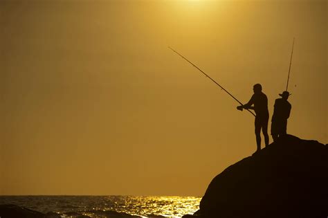 Silhouette Photo Of Two Men Holding Fishing Rods Against Body Of Water