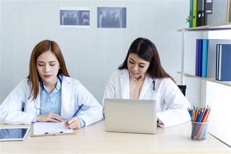 two asian women doctors discuss meeting doctor`s office medical clinic using laptop consulting