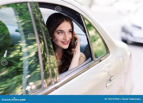 A Young Girl Is Sitting In The Back Seat Of A Car And Is Talking On The
