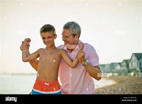 Young Boy Has Fun Flexing His Muscles With His Father On The Beach At