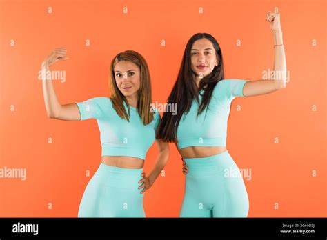 Fitness Girls Flexing Biceps And Smiling Studio Shot With Orange