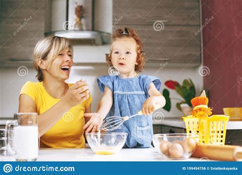 Happy Mom And Her Little Daughter Are Cooking In The Kitchen The Girl Whips Eggs In A Glass