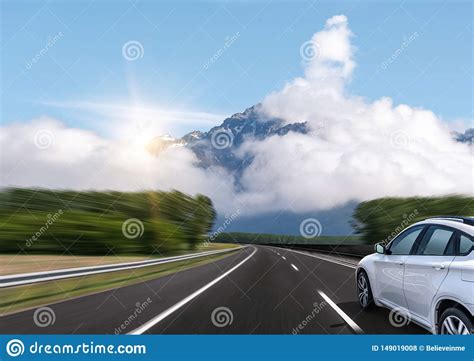 The Car Drives Fast On The Highway Against The Backdrop Of A Mountain