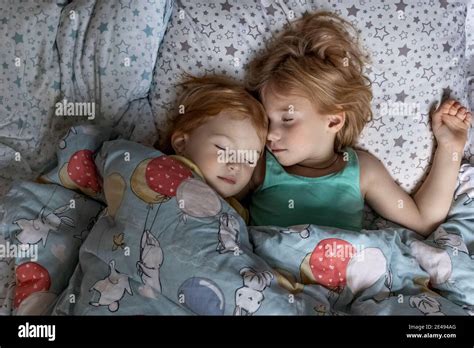 Two Little Sibling Girls Sisters Sleeping In An Embrace In Bed Under