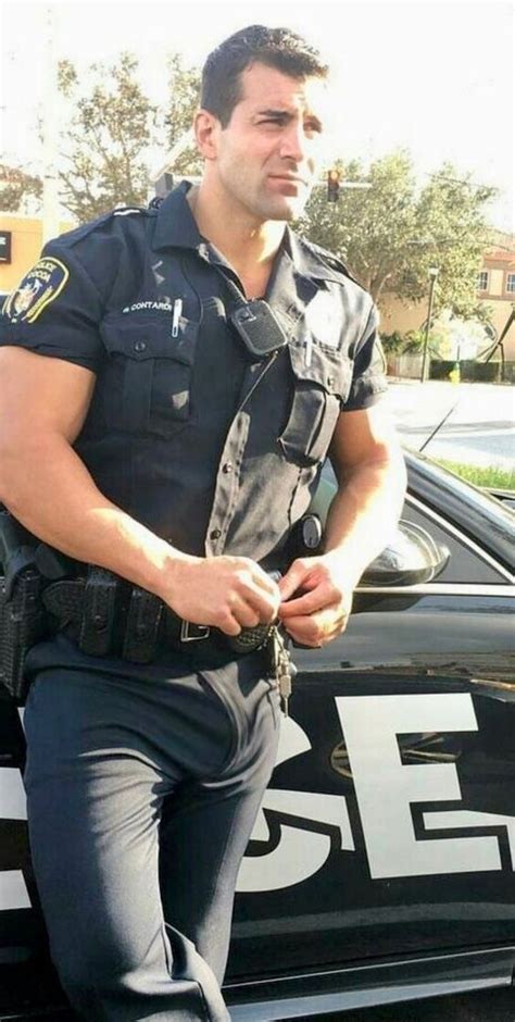 A Police Officer Is Standing In Front Of His Patrol Car And Looking At The Camera