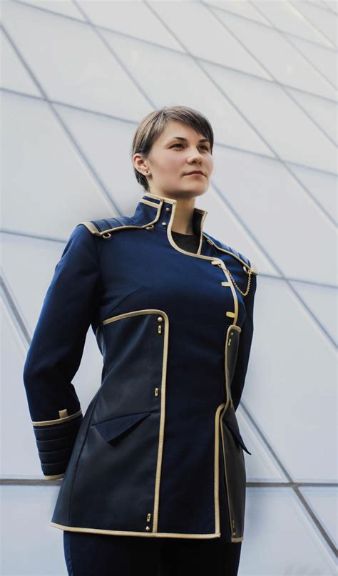 A Woman Wearing A Blue Uniform Standing In Front Of A Building With Her Hands On Her Hips