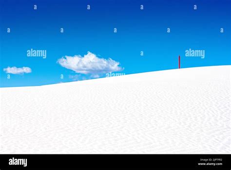 Single Red Marker Standing On White Dune With Puffy Cloud In The Sky In