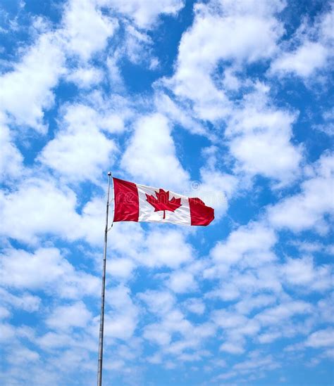 Large Canadian Flag Flying Against Blue Sky Background Stock Photo